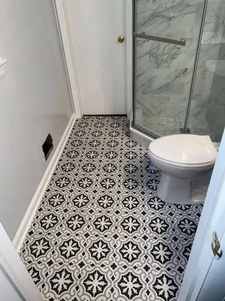 Remodeled bathroom with patterned black and white tile floor and glass shower